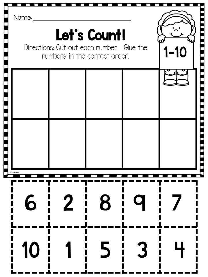 A young student carefully using safety scissors to cut out numbers from a worksheet